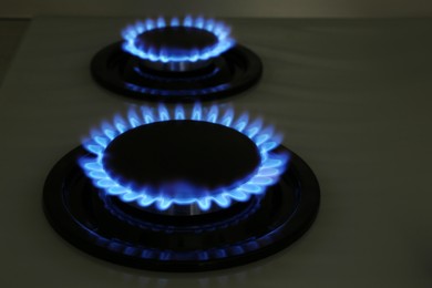 Photo of Modern gas cooktop with burning blue flames in kitchen at night