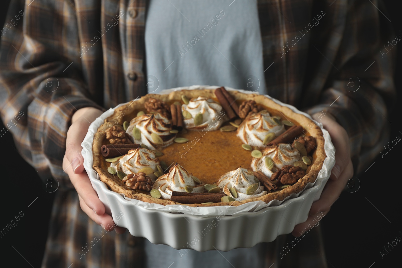 Photo of Woman holding homemade pumpkin pie with whipped cream, seeds and cinnamon on black background, closeup