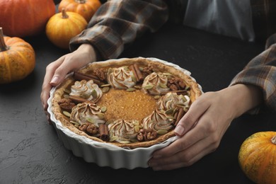 Woman with homemade pumpkin pie with whipped cream, seeds and cinnamon at black table, closeup