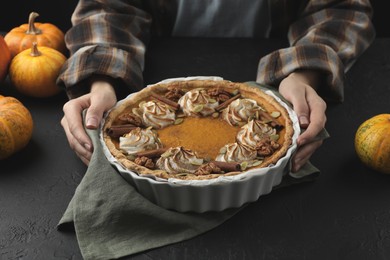 Woman with homemade pumpkin pie with whipped cream, seeds and cinnamon at black table, closeup