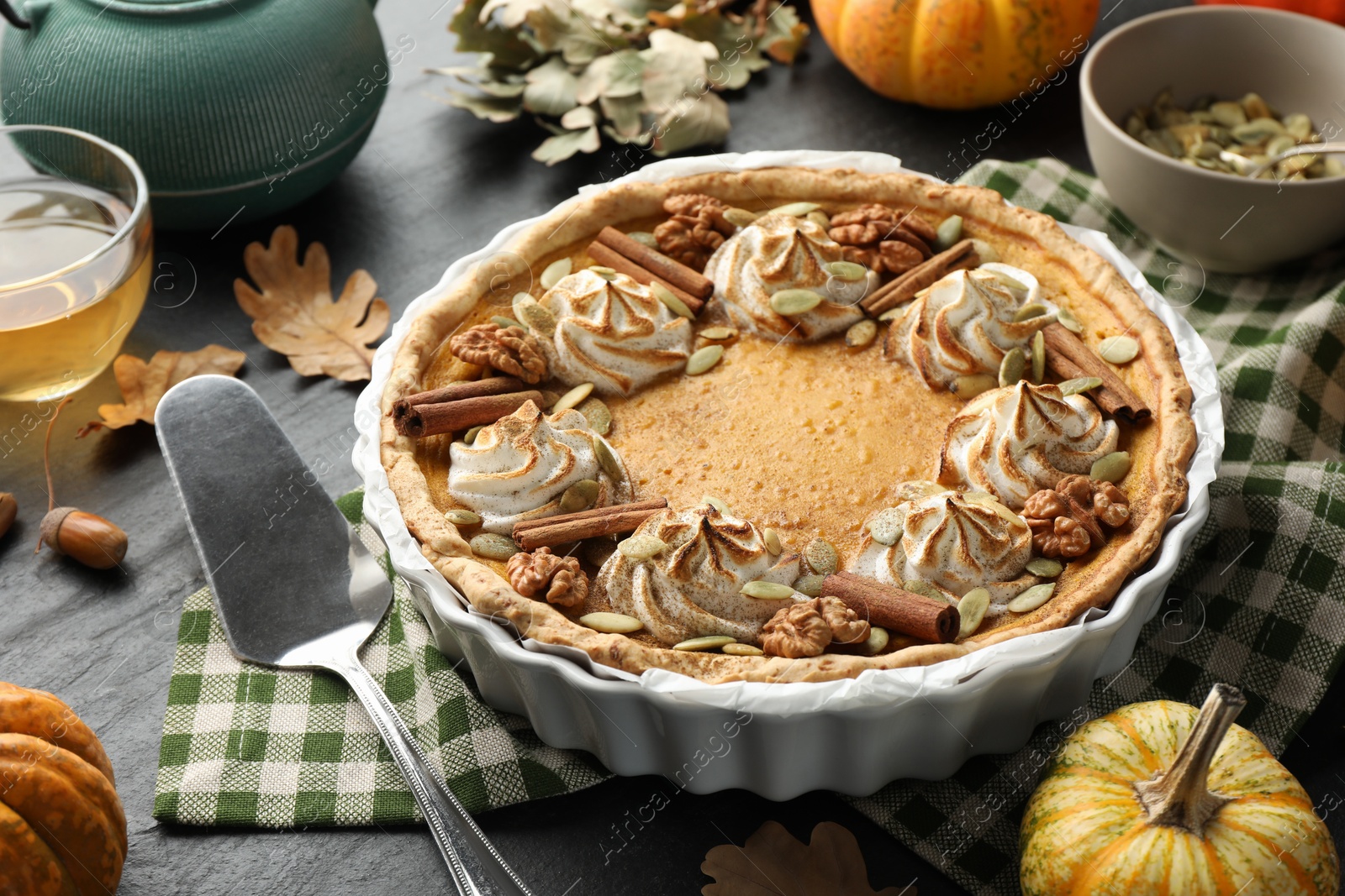 Photo of Homemade pumpkin pie with whipped cream, seeds and cinnamon on grey table