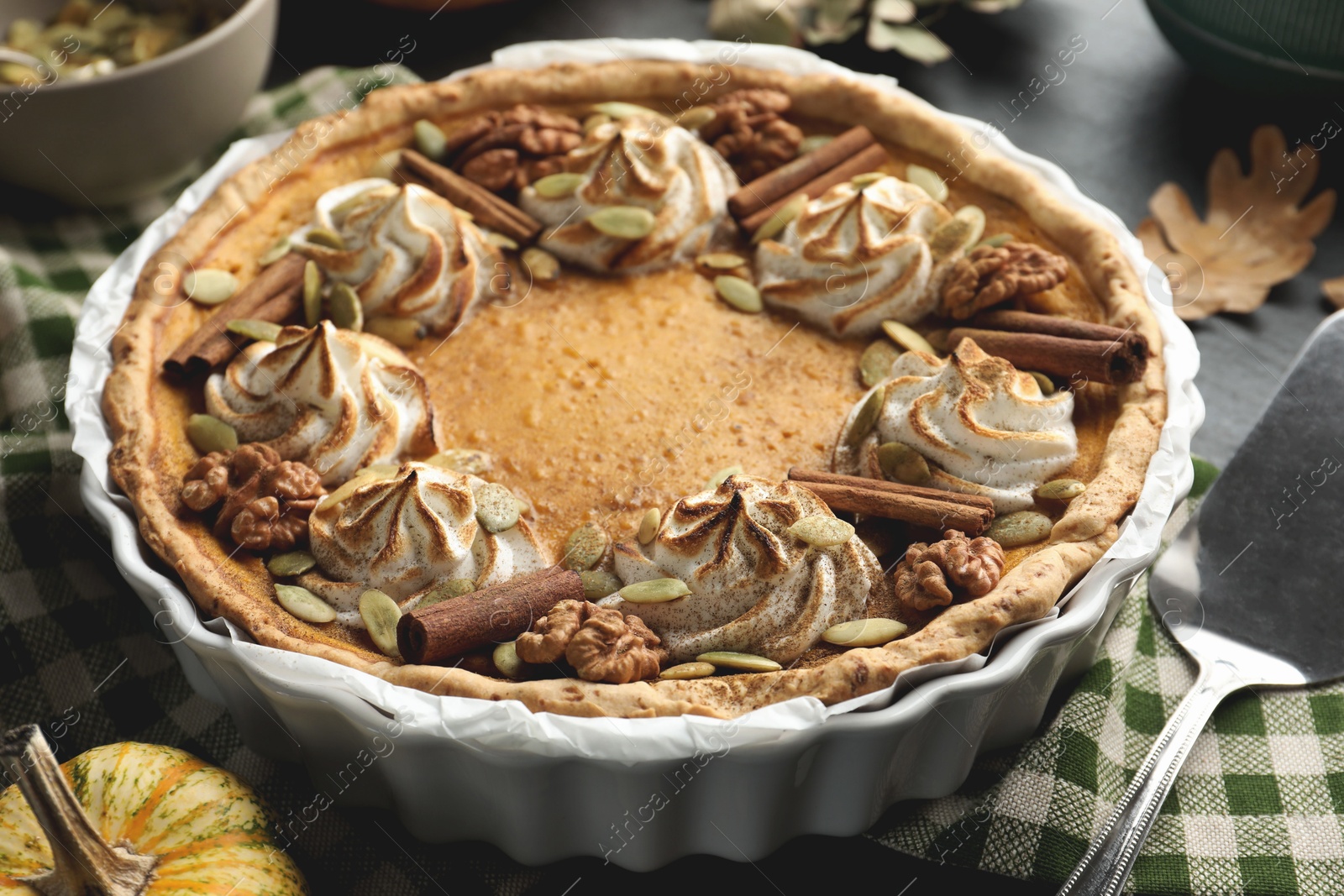 Photo of Homemade pumpkin pie with whipped cream, seeds and cinnamon on grey table, closeup