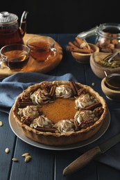 Photo of Homemade pumpkin pie with whipped cream, seeds and cinnamon on blue wooden table