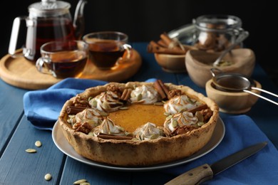 Photo of Homemade pumpkin pie with whipped cream, seeds and cinnamon on blue wooden table