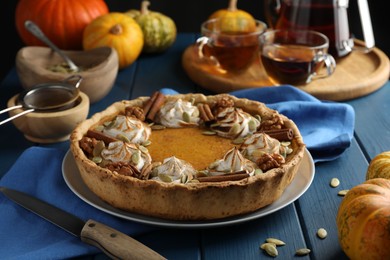 Photo of Homemade pumpkin pie with whipped cream, seeds and cinnamon on blue wooden table