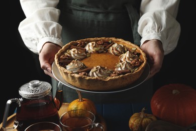 Photo of Woman with homemade pumpkin pie with whipped cream, seeds and cinnamon at blue wooden table, closeup