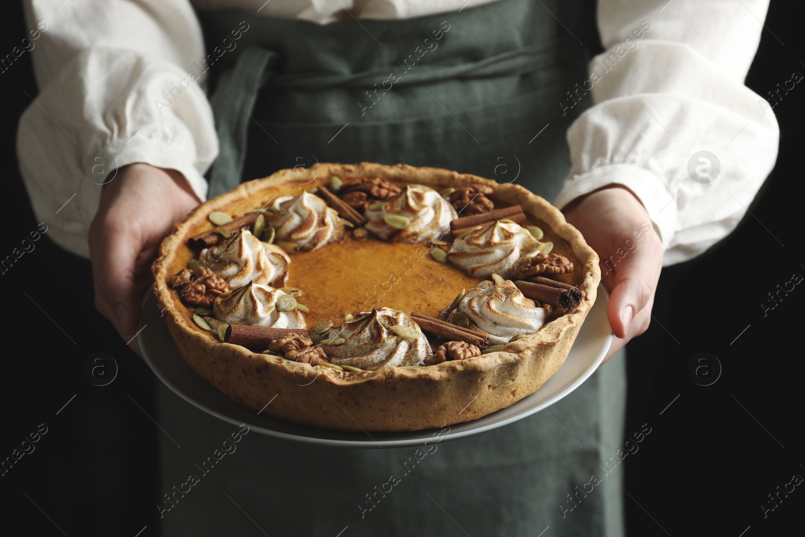 Photo of Woman holding homemade pumpkin pie with whipped cream, seeds and cinnamon on black background, closeup