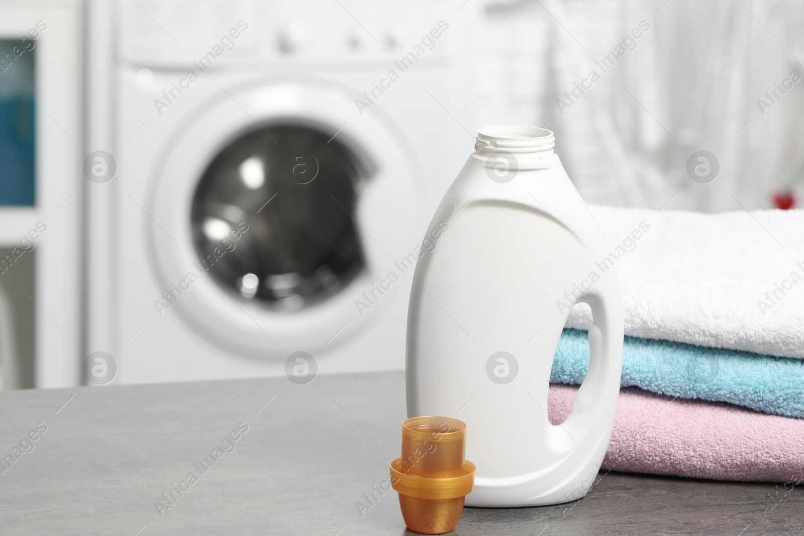 Photo of Laundry detergent, cap and stacked clean towels on grey table, space for text