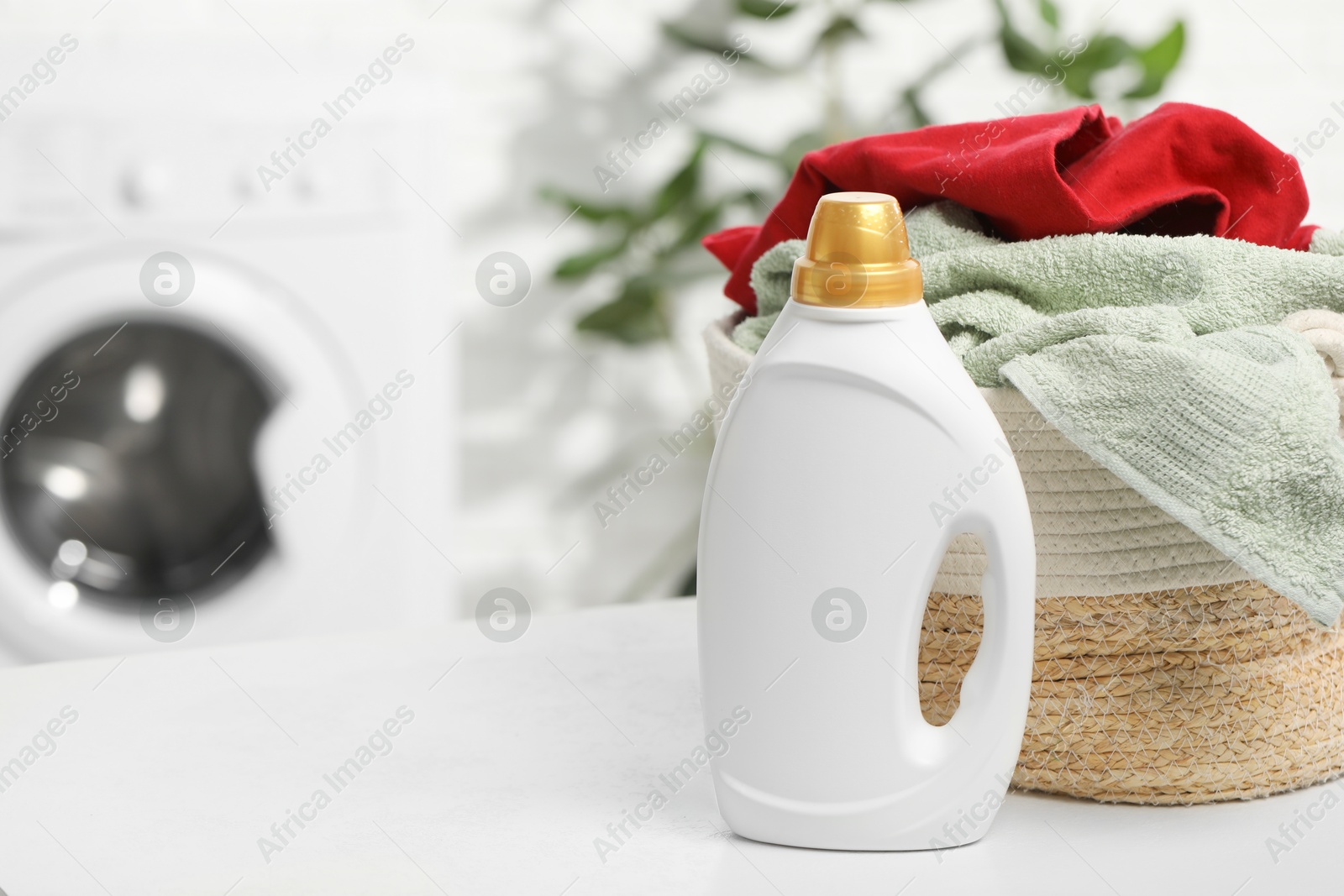 Photo of Detergent and basket with towels on white table in bathroom, space for text