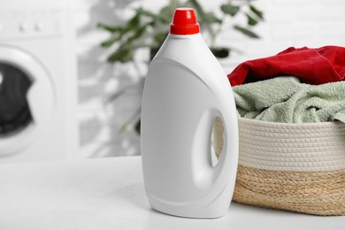 Photo of Detergent and basket with towels on white table in bathroom, space for text