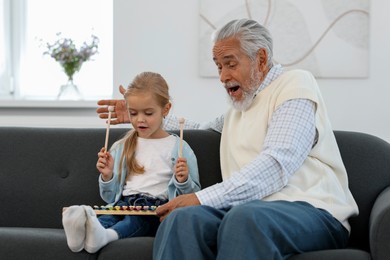 Photo of Grandpa and his granddaughter playing toy xylophone on sofa at home