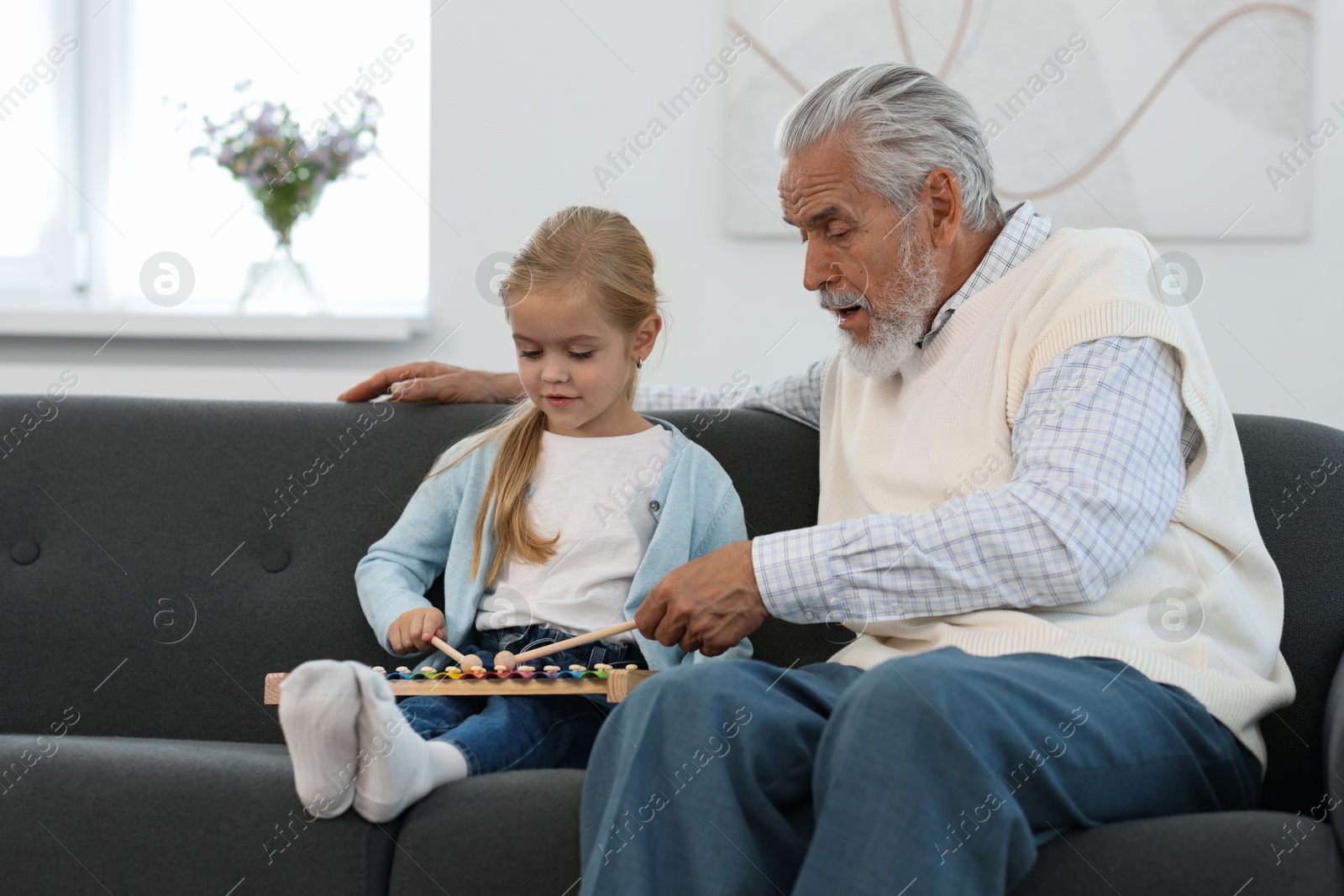 Photo of Grandpa and his granddaughter playing toy xylophone on sofa at home