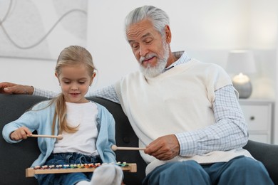 Photo of Grandpa and his granddaughter playing toy xylophone on sofa at home