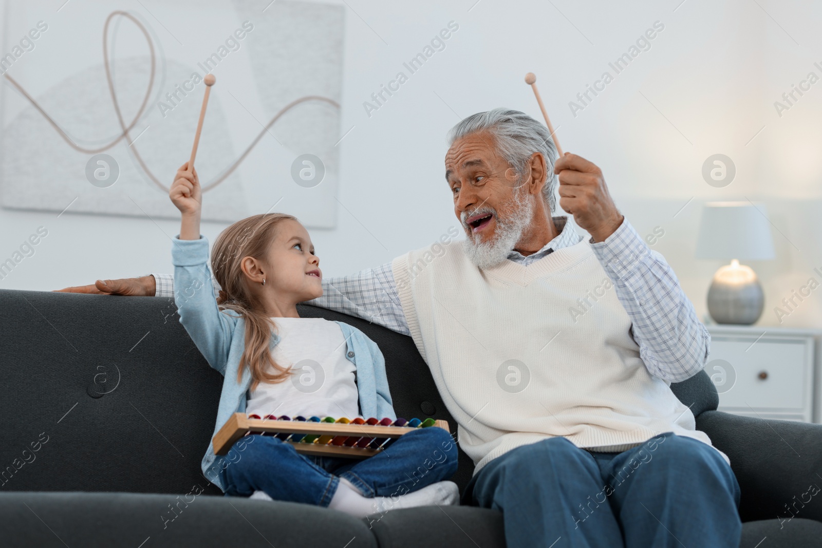 Photo of Grandpa and his granddaughter playing toy xylophone on sofa at home