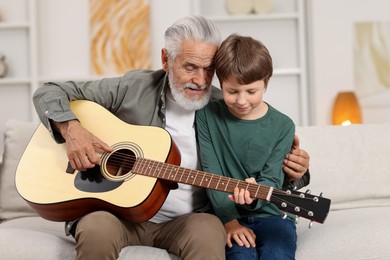 Photo of Grandpa teaching his grandson to play guitar on sofa at home