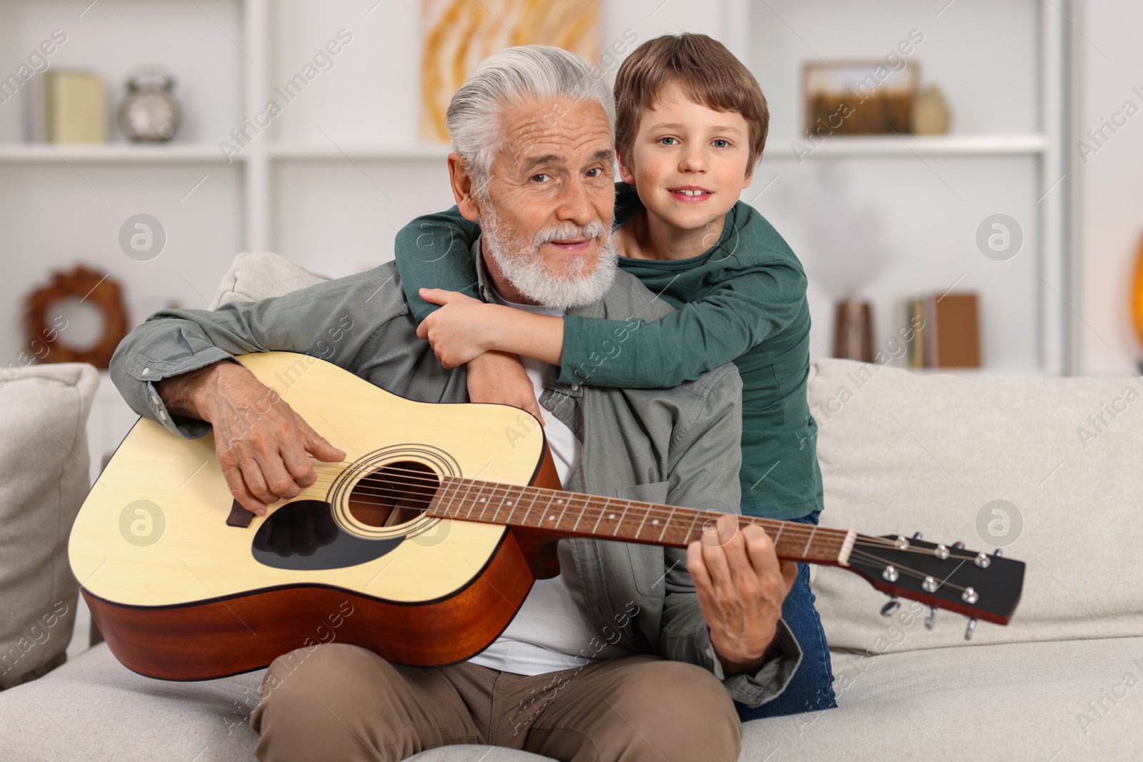 Photo of Grandpa teaching his grandson to play guitar on sofa at home