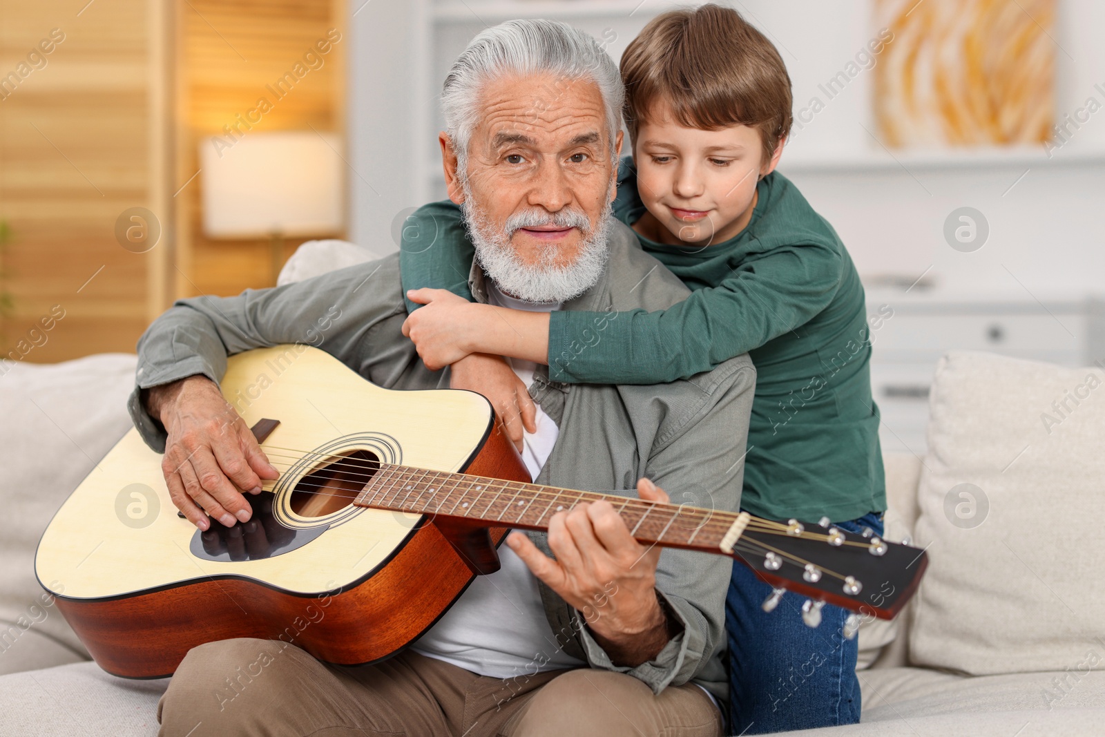 Photo of Grandpa teaching his grandson to play guitar on sofa at home