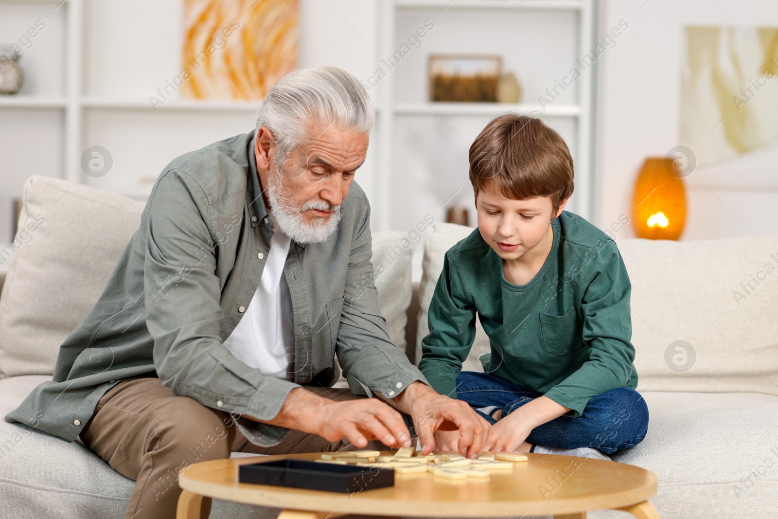 Photo of Grandpa and his grandson playing dominoes at table indoors