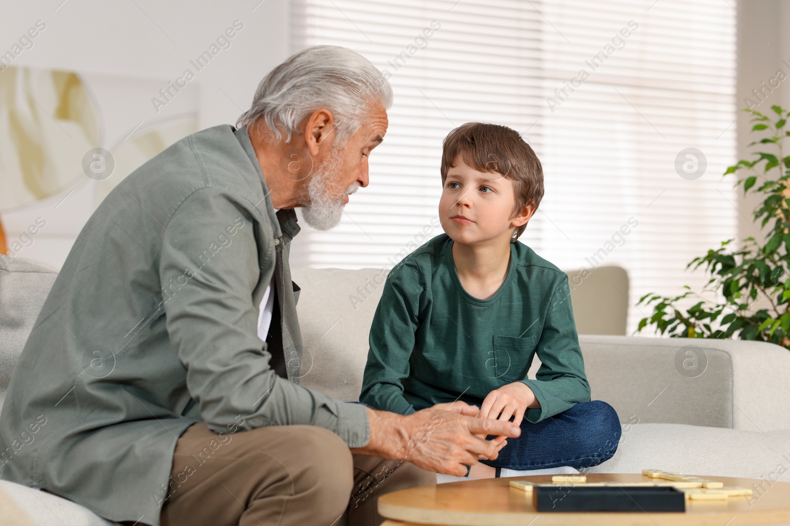 Photo of Grandpa and his grandson playing dominoes at table indoors