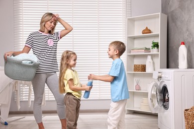 Tired housewife doing laundry while her kids playing indoors