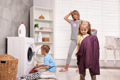 Tired housewife and her kids doing laundry together in bathroom