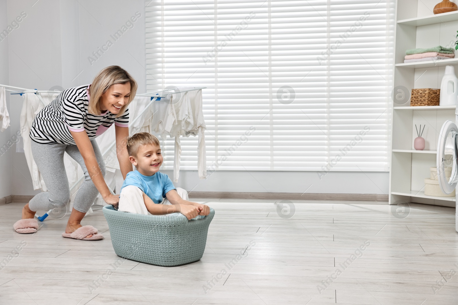 Photo of Happy housewife and her son playing together in laundry room, space for text