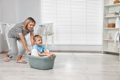 Happy housewife and her son playing together in laundry room, space for text