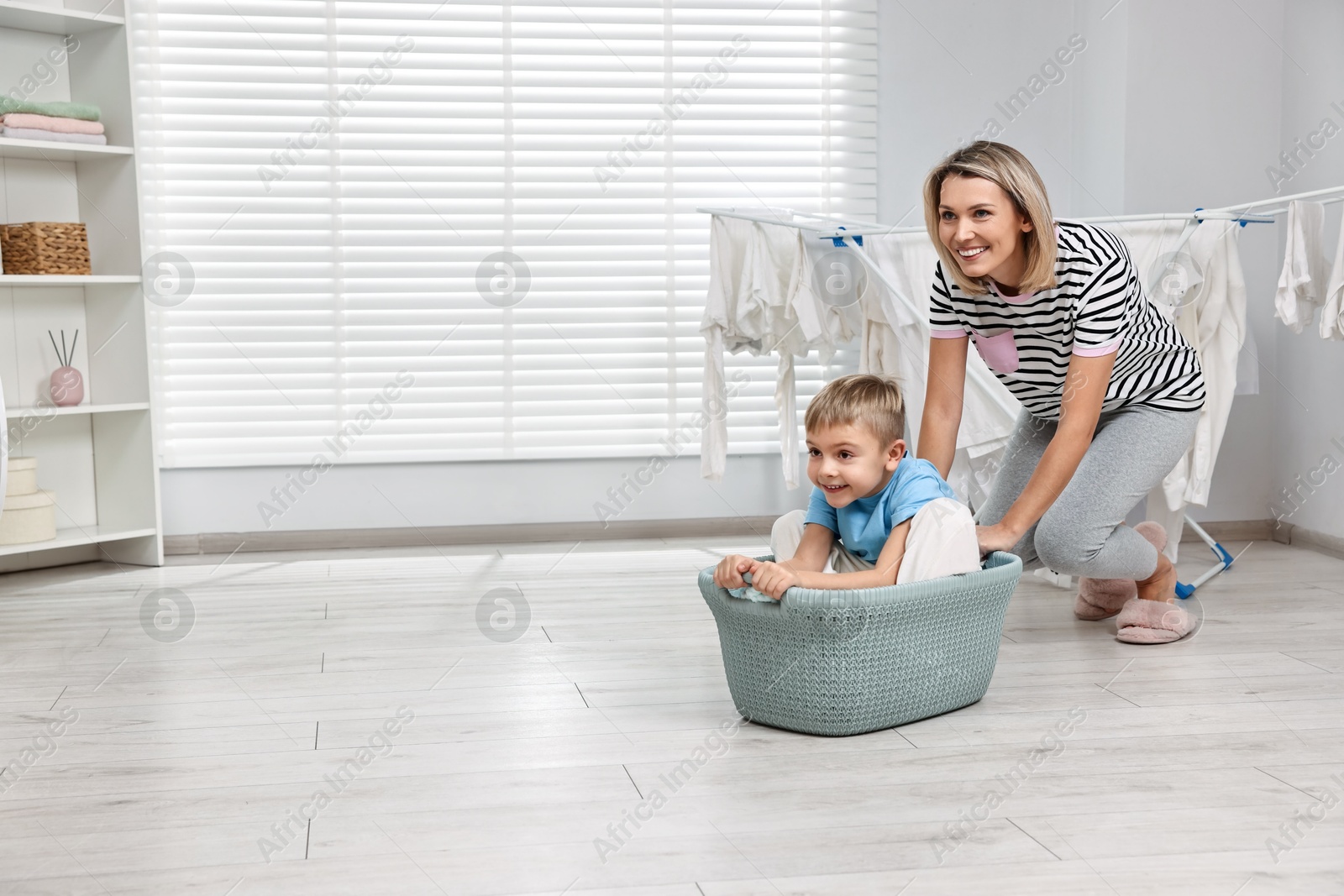 Photo of Happy housewife and her son playing together in laundry room, space for text