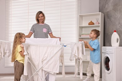 Photo of Happy housewife and her kids doing laundry together at home