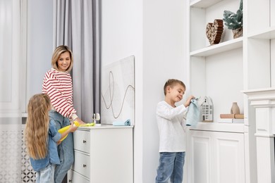 Happy housewife and her kids cleaning room together