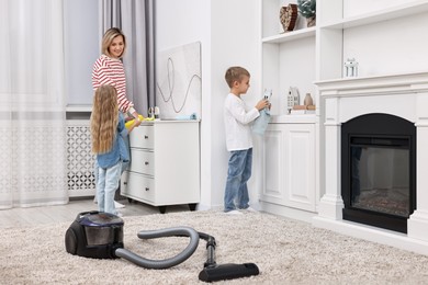 Happy housewife and her kids cleaning room together