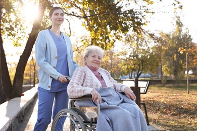 Photo of Caregiver with elderly woman in wheelchair at park. Space for text