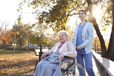 Photo of Caregiver with elderly woman in wheelchair at park. Space for text