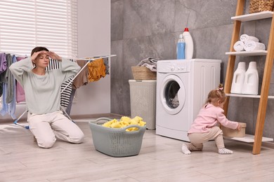 Photo of Tired housewife with her little daughter resting after doing laundry at home