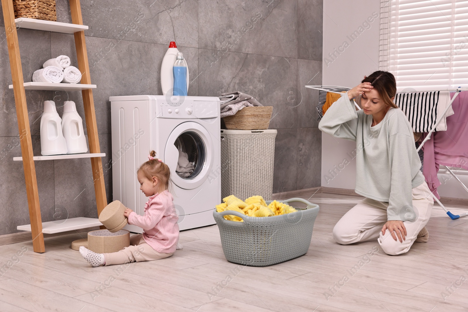 Photo of Tired housewife with her little daughter resting after doing laundry at home