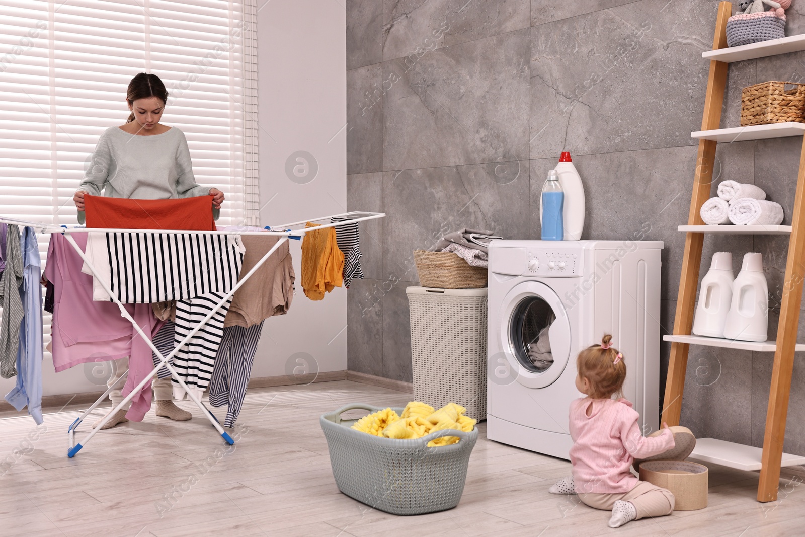 Photo of Housewife hanging clothes on drying rack while her daughter playing at home