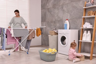 Photo of Housewife hanging clothes on drying rack while her daughter playing at home