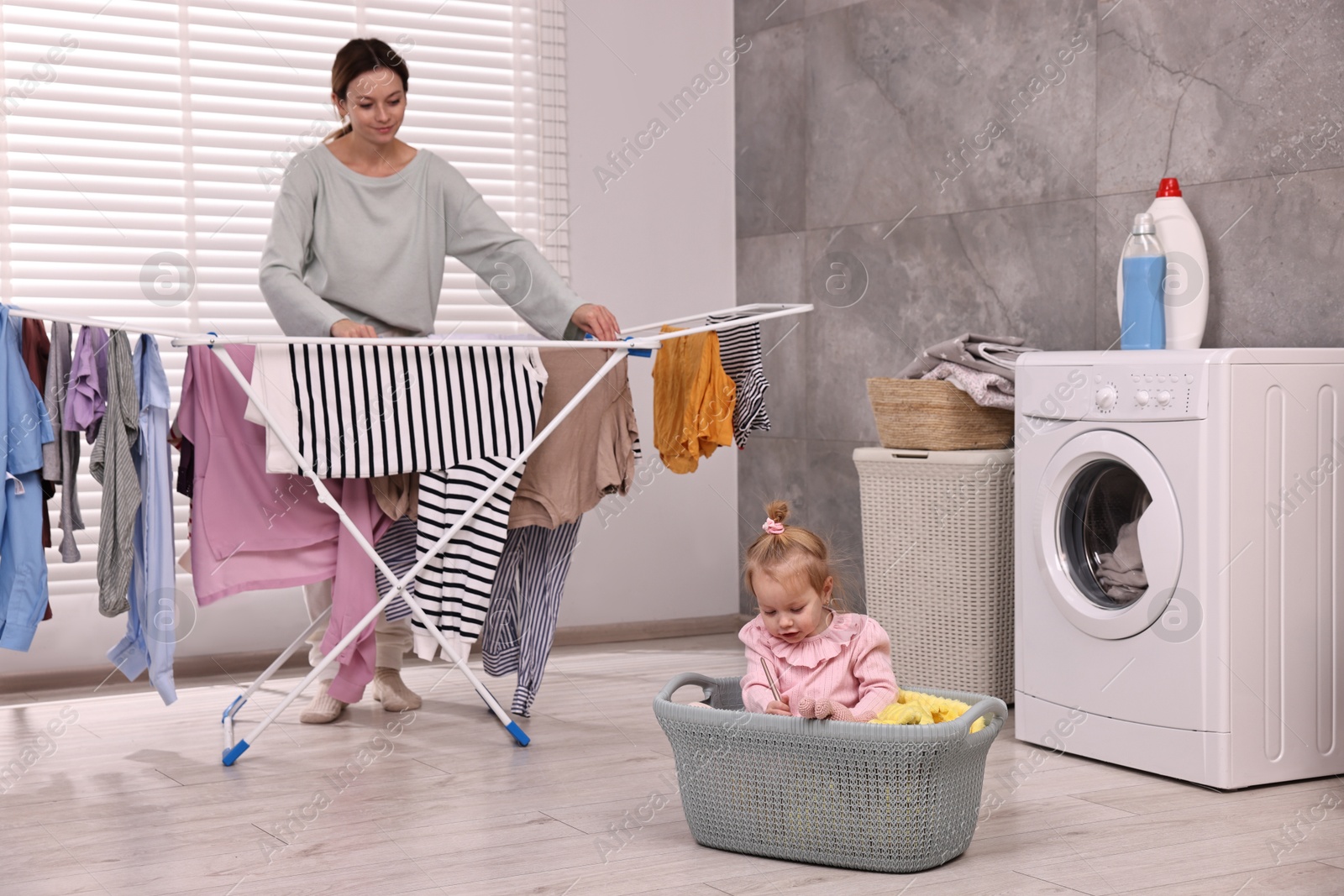 Photo of Housewife hanging clothes on drying rack while her daughter playing at home