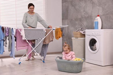 Housewife hanging clothes on drying rack while her daughter playing at home