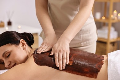 Woman undergoing chocolate body wrap treatment in spa salon