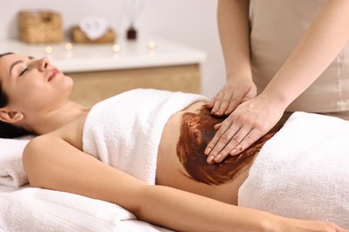 Woman undergoing chocolate body wrap treatment in spa salon