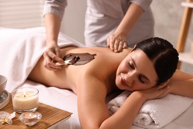 Photo of Chocolate body wrap. Spa worker applying mask onto woman's back in salon, closeup