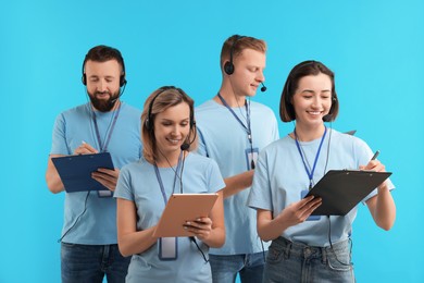 Photo of Technical support call center. Team of friendly operators working on light blue background