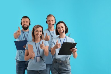 Technical support call center. Team of smiling operators showing thumbs up on light blue background. Space for text