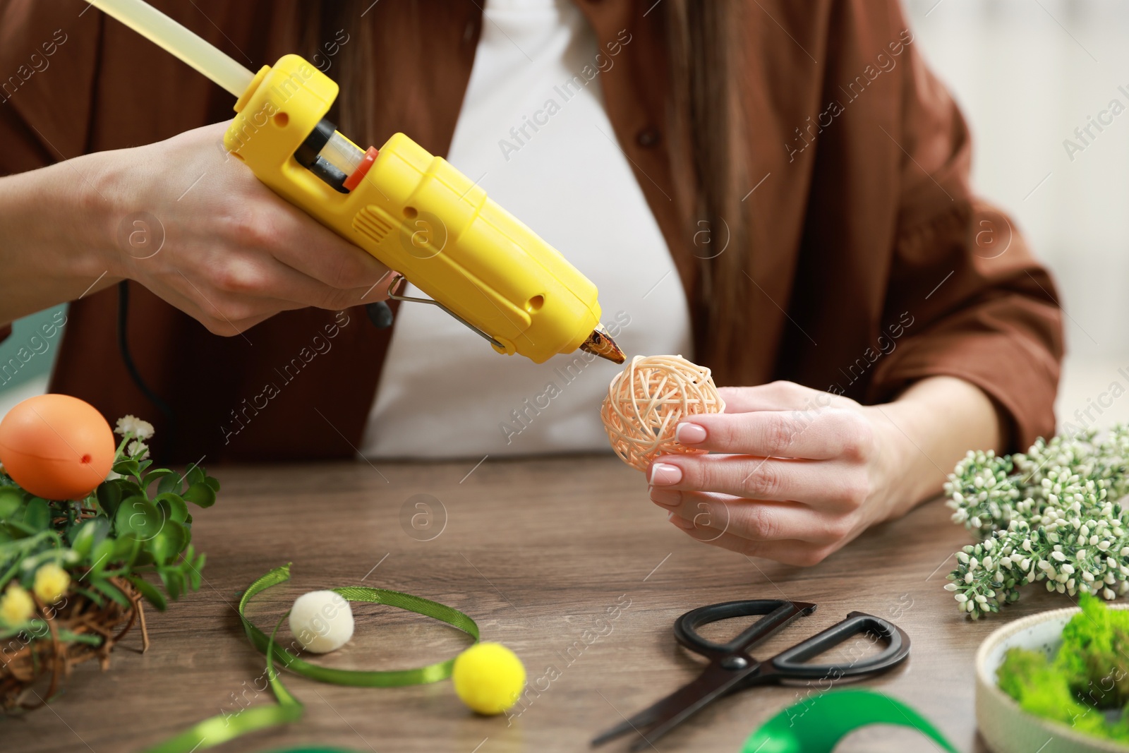 Photo of Woman with hot glue gun making craft at table indoors, closeup