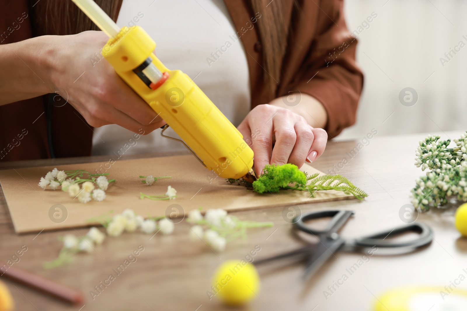 Photo of Woman with hot glue gun making craft at table indoors, closeup