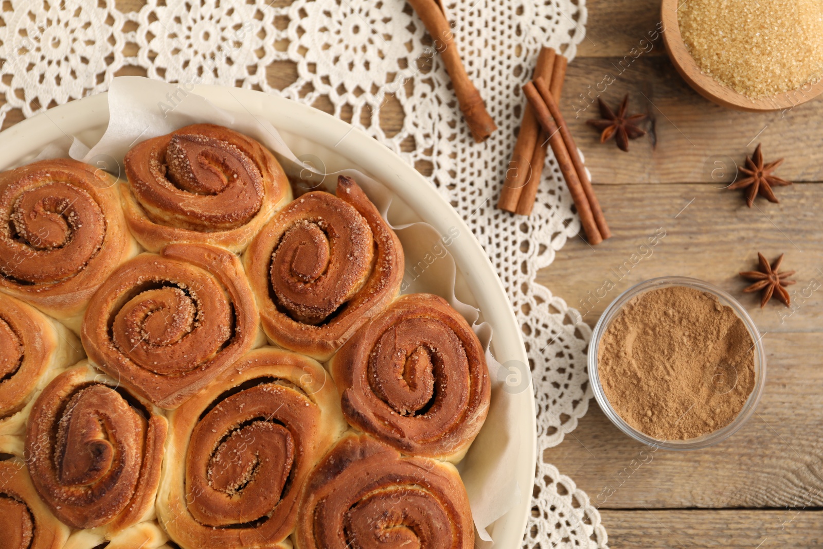 Photo of Freshly baked cinnamon rolls and spices on wooden table, flat lay