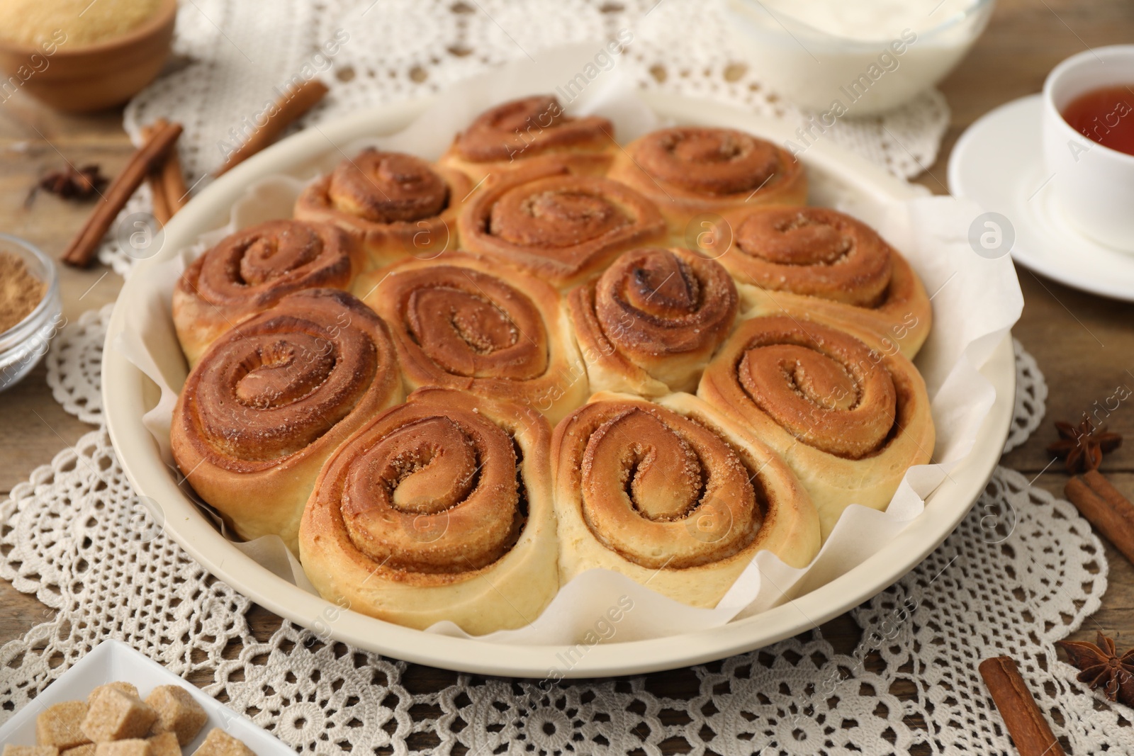 Photo of Freshly baked cinnamon rolls and spices on wooden table, closeup