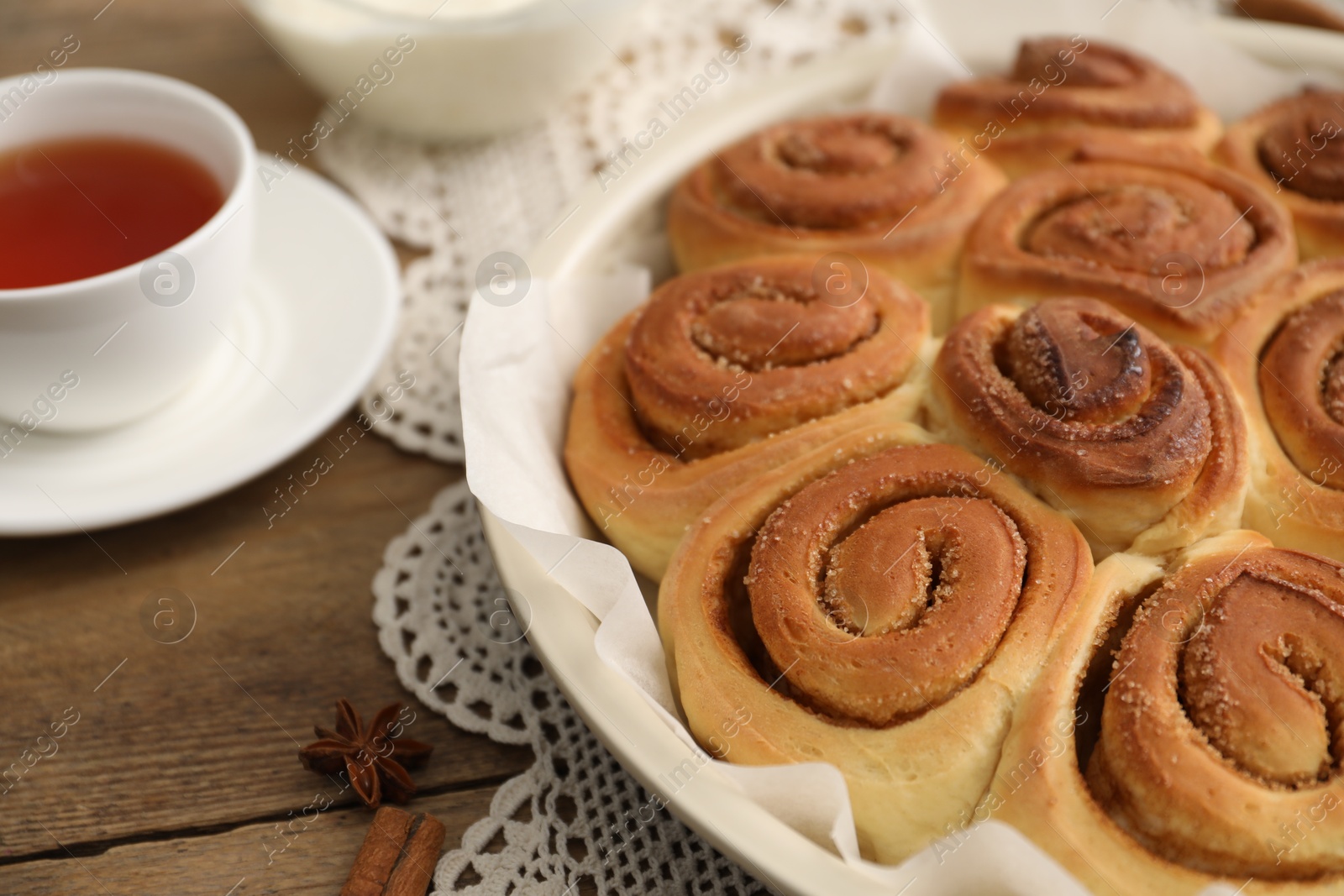 Photo of Freshly baked cinnamon rolls and tea on wooden table, closeup