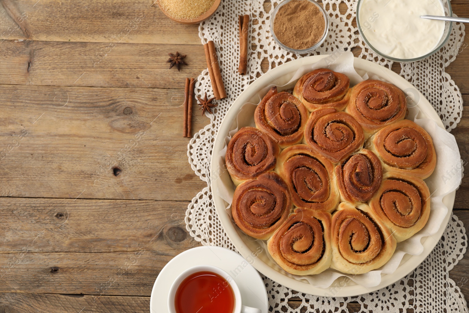 Photo of Freshly baked cinnamon rolls, tea and spices on wooden table, flat lay. Space for text